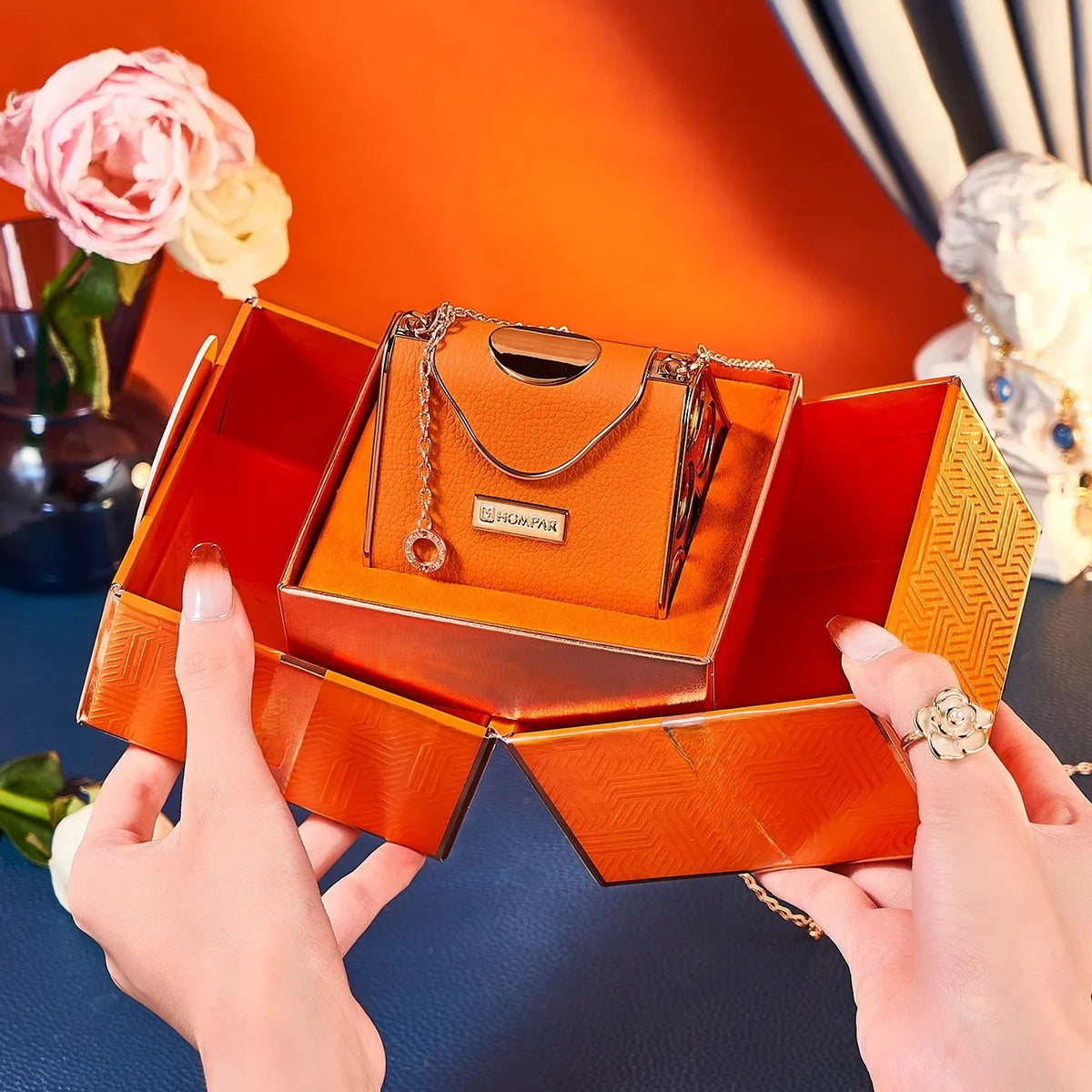 Orange leather chain bag open showing 5 velvet matte lipsticks in individual gold-capped side slots — held in hands with gold chain strap visible