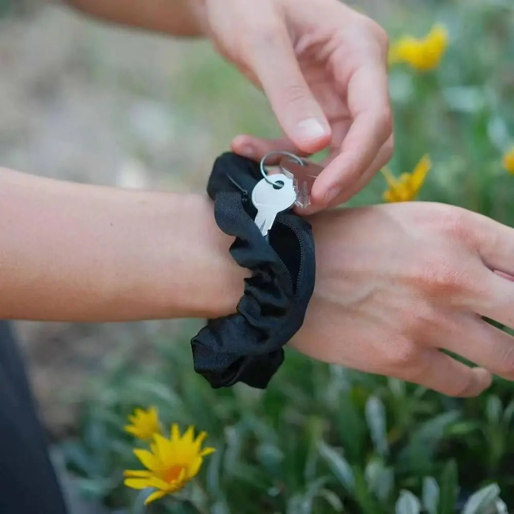Hidden closure hair scrunchie worn on wrist showing zipper pocket with keys being removed outdoors