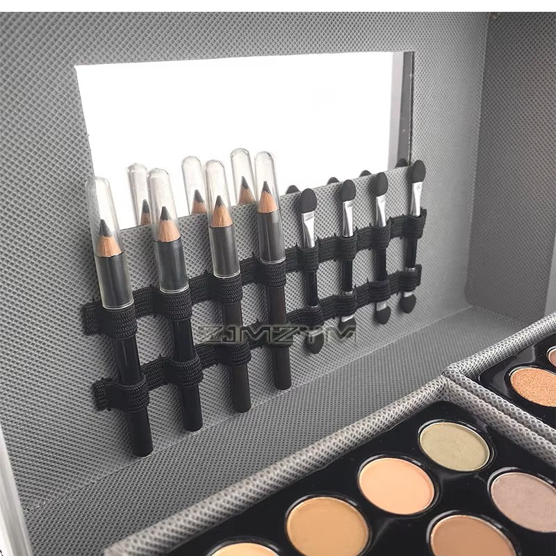 Close-up of the train case lid interior with mirror, eyebrow pencils, lip liners and sponge applicator sticks held in elastic straps