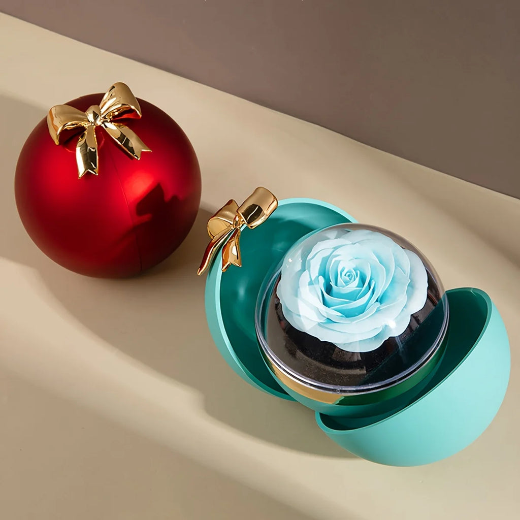 Blue ball-style jewellery box open with the rose displayed under a clear dome in the lid, beside a closed red ball box with a gold-tone bow
