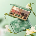 Plantism eyeshadow palette open and closed — jade green botanical compact with 10 warm neutral shades and brush, styled with white flowers