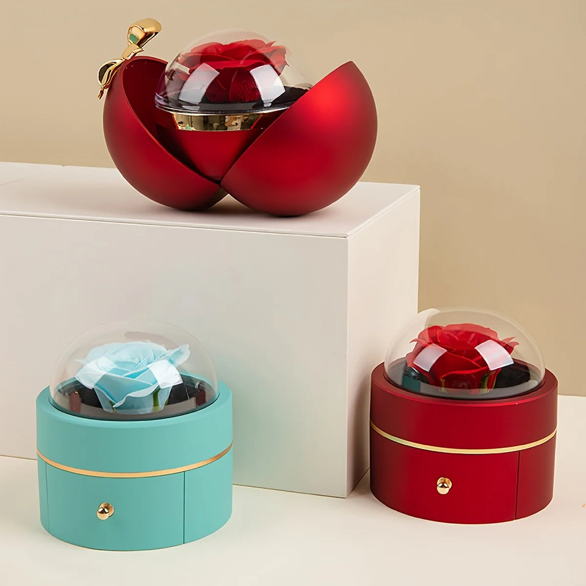 Red ball-style jewellery box open on a plinth showing the rose dome inside, beside closed blue and red round rose box styles