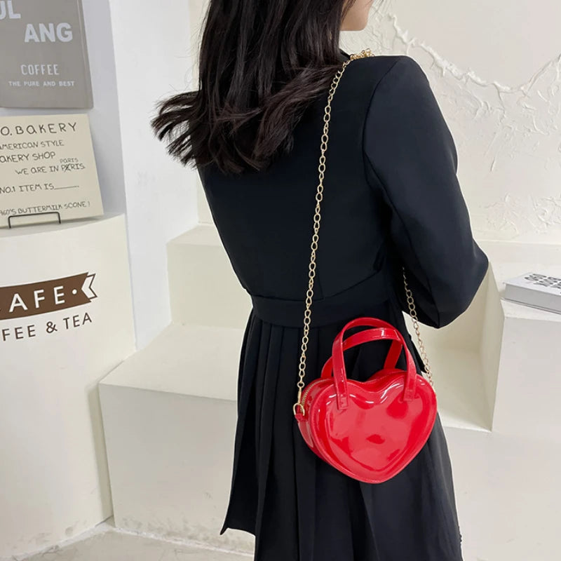Red heart-shaped bag worn crossbody with the gold chain strap