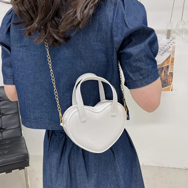 White heart-shaped bag worn crossbody with the gold chain strap