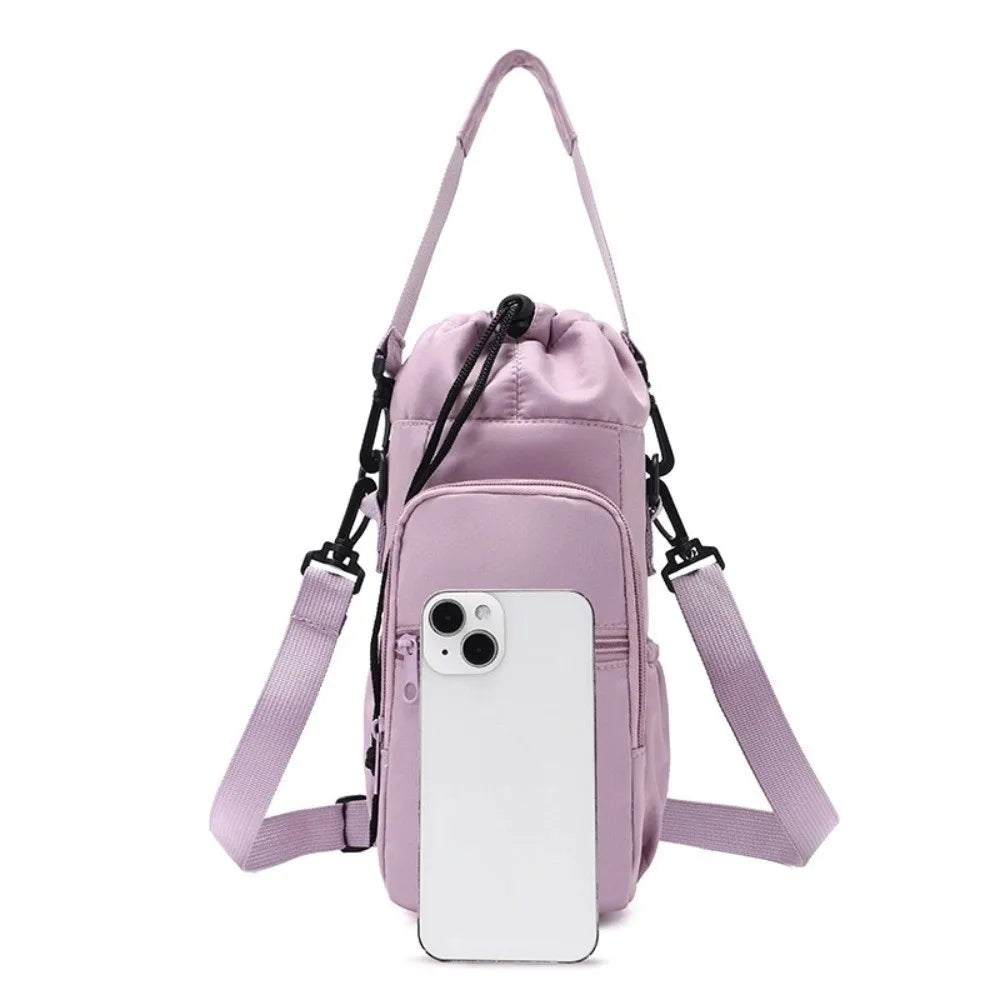 A light purple drawstring backpack with a front zippered pocket, adjustable shoulder straps, and black plastic hardware, shown against a plain white background with a white smartphone placed in front for scale.