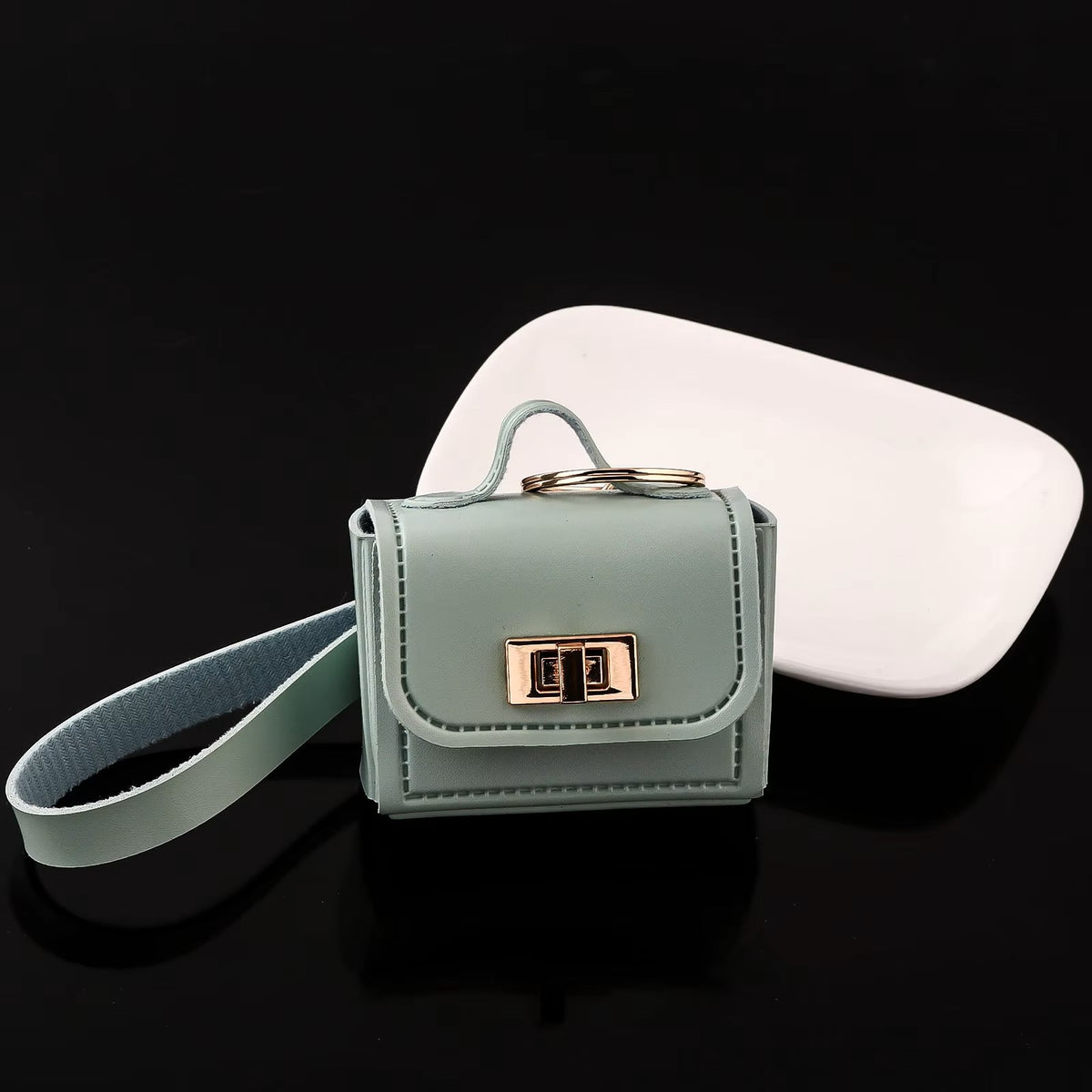 Green kawaii mini bag charm keychain with wrist strap shown next to AirPods case for size reference