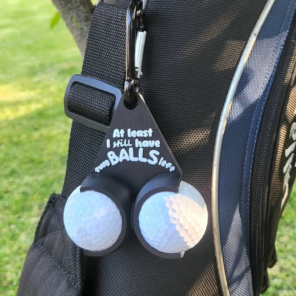 Novelty golf ball holder with two white golf balls clipped to black golf bag strap on course