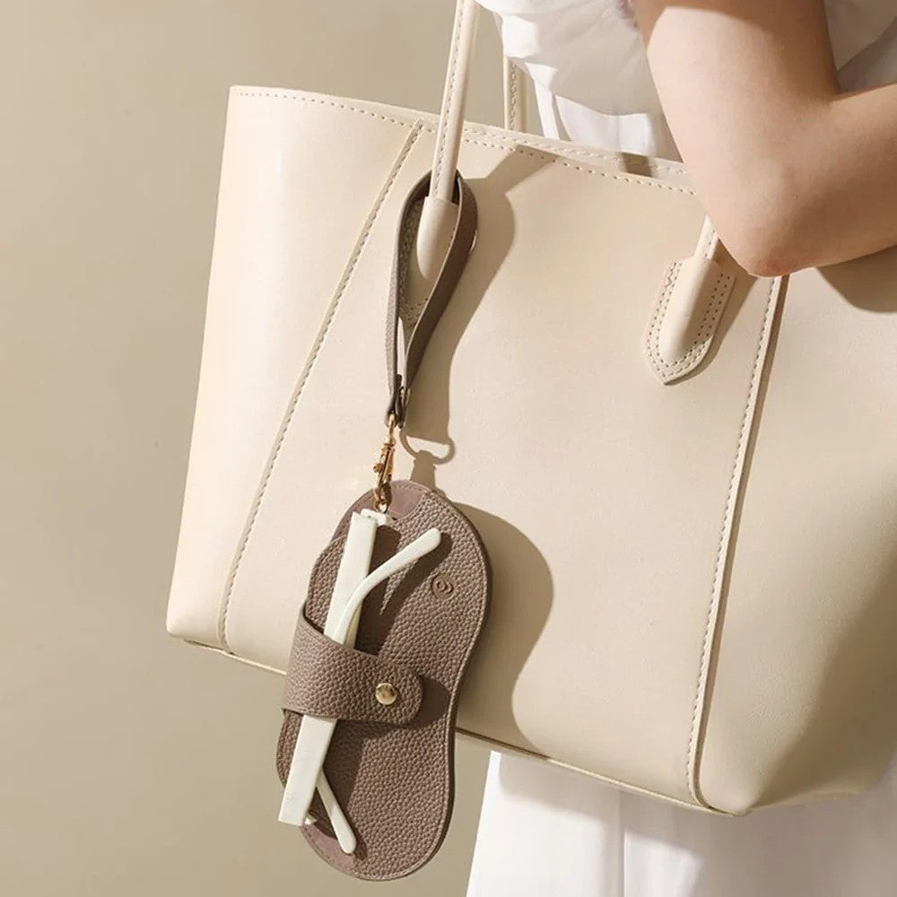 MiniSolutions oval glasses case in brown hanging from a cream tote bag handle by wrist strap